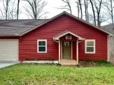 A red house with a garage in the woods.