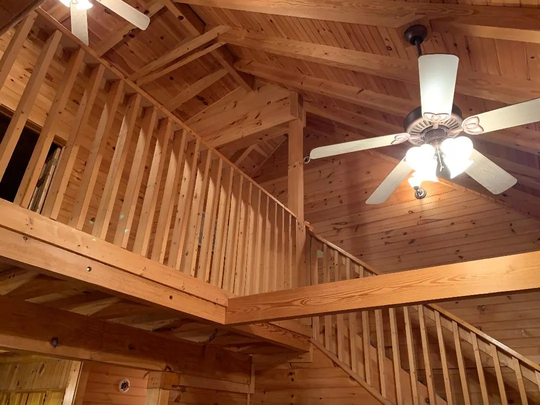 The inside of a log cabin with a fan and stairs.