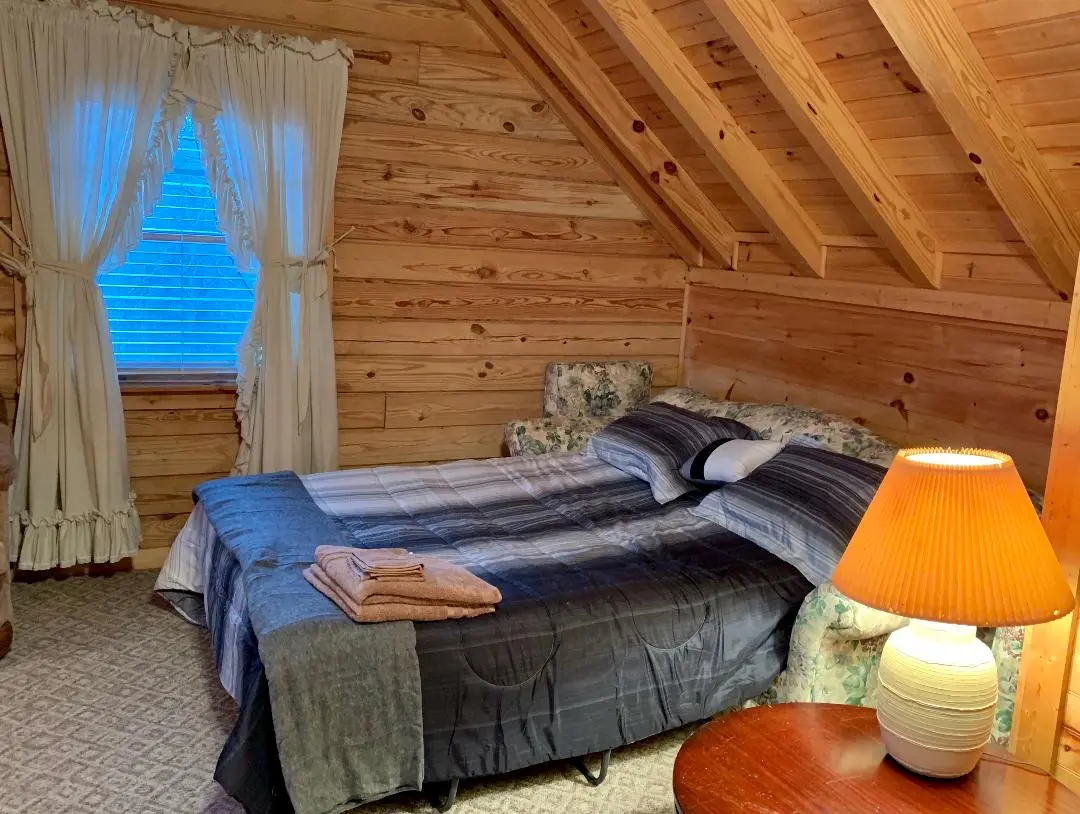 A bedroom in a log cabin with a bed and a lamp.