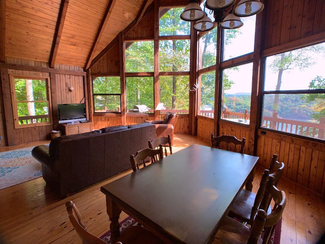 A living room with large windows and a dining table.