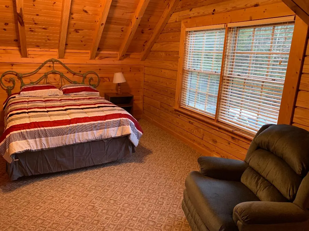 A bedroom in a log cabin with a bed and chair.