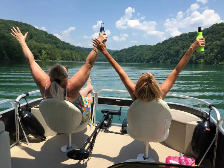 Two women on a boat with their arms raised.