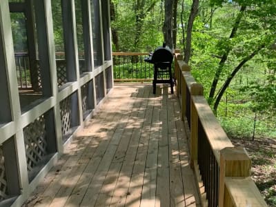 A wooden deck with a grill in the woods.