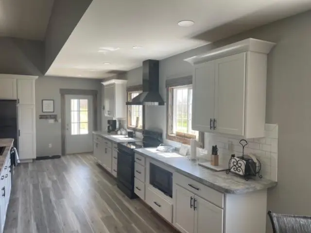 A kitchen with white cabinets and wood floors.