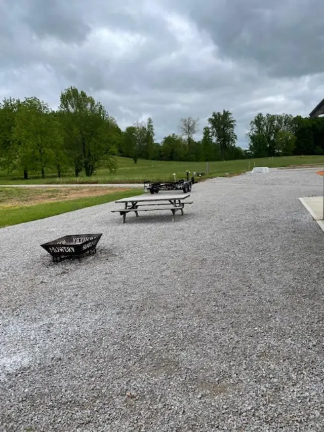 A gravel parking lot with picnic tables and a fire pit.