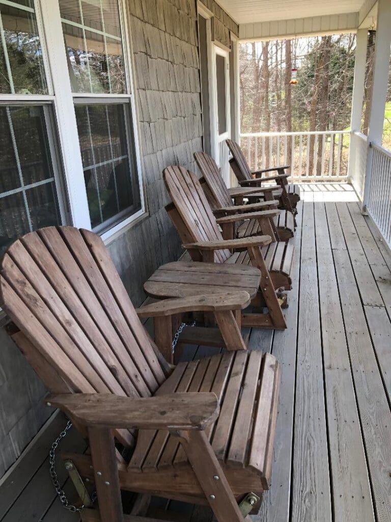 Four wooden adirondack chairs on a porch.