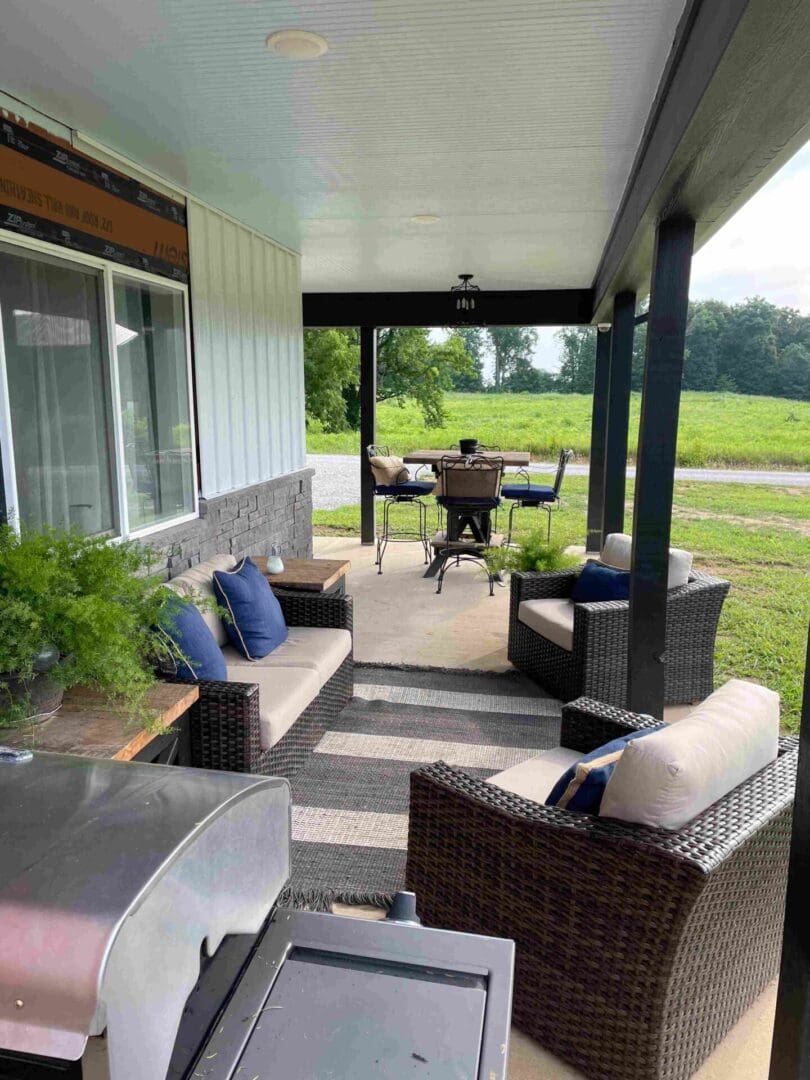 A covered outdoor patio with wicker furniture and a dining set overlooking a grassy area.