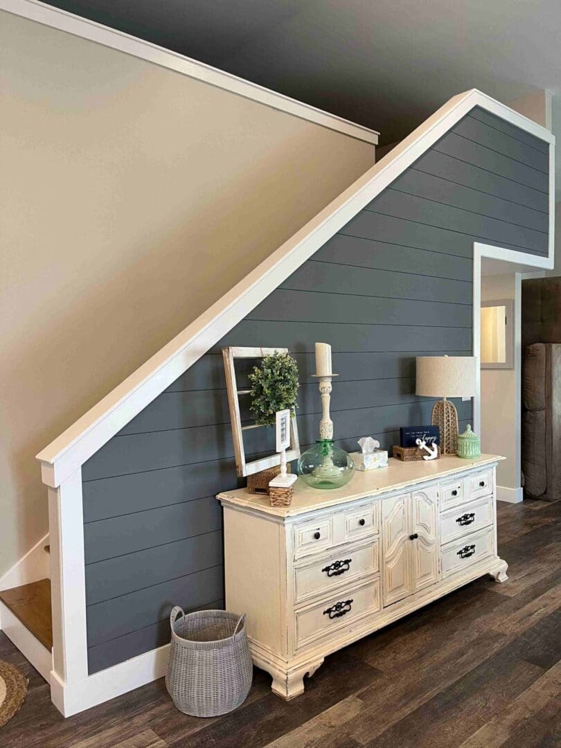 A vintage-style wooden console table with decorative items placed beneath a staircase with a dark blue accent wall.