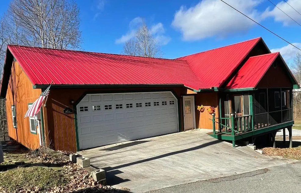 A wooden house with a red roof, an attached garage, and an american flag displayed on the front.