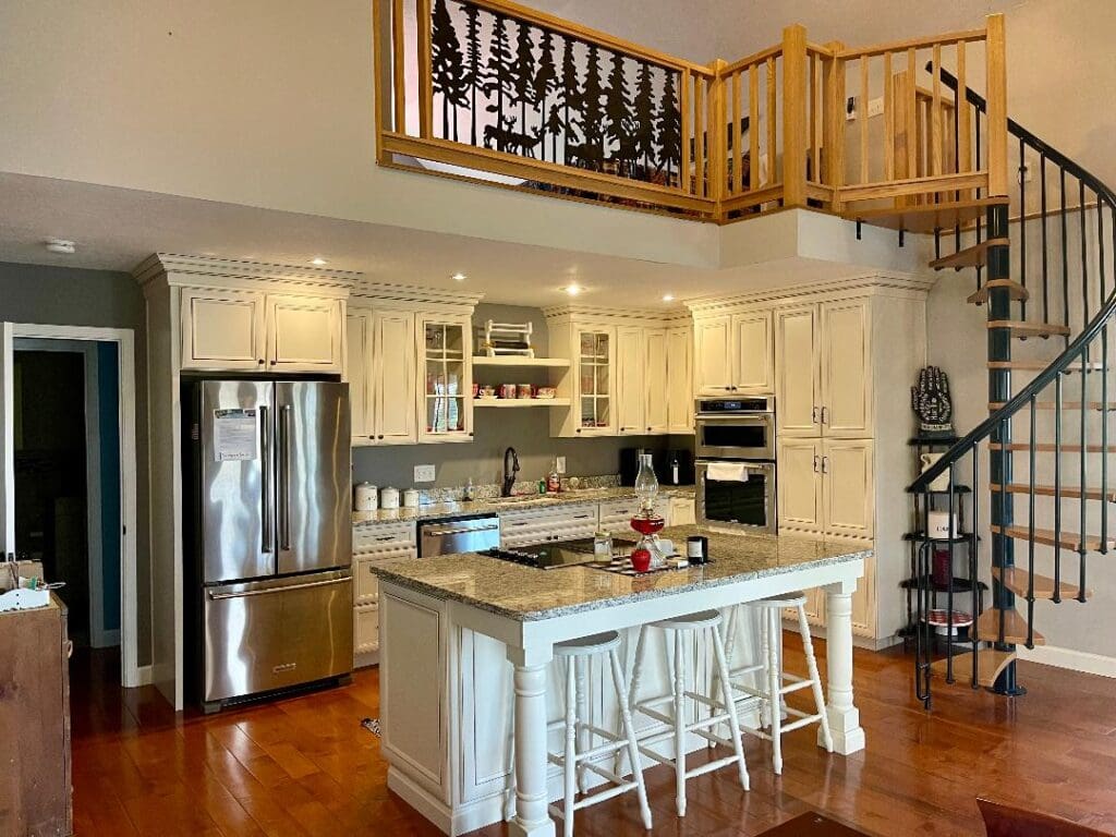 Modern kitchen interior with stainless steel appliances, white cabinets, and a spiral staircase leading to an upper level.