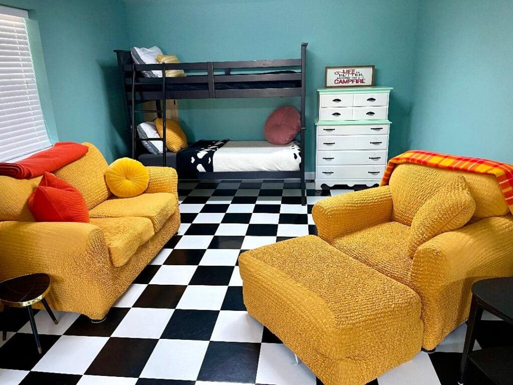 A vibrant children's room with a blue bunk bed, yellow armchairs, and black and white checkered floor.