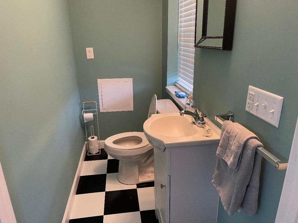 A neat and tidy bathroom with teal walls, white fixtures, and checkered flooring.