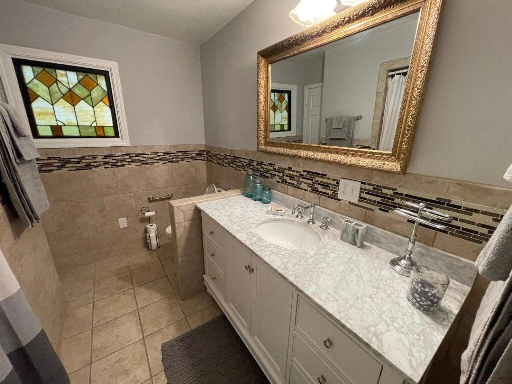 A well-lit modern bathroom with a white vanity, marble countertop, and decorative tiled backsplash.