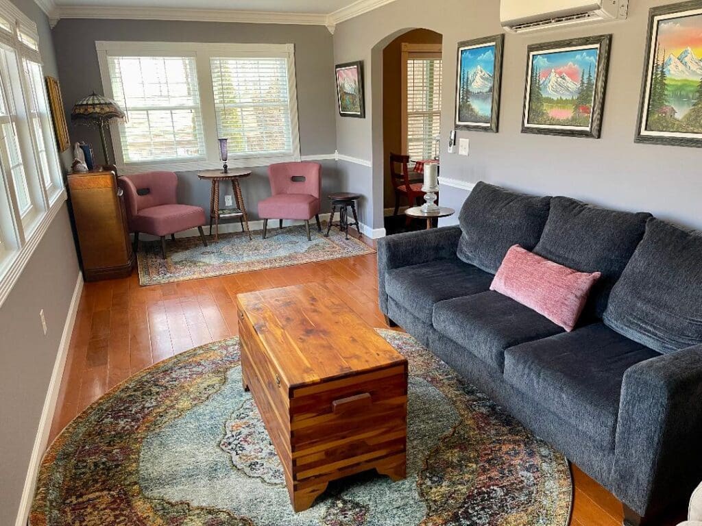 A cozy living room with a gray sofa, wooden coffee table, and a dining area in the background.