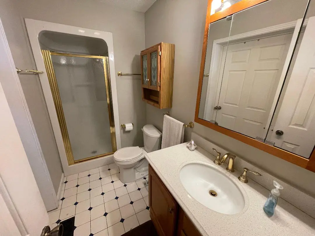 A small bathroom interior featuring a toilet, sink with vanity, and mirrored medicine cabinet with tiled flooring.