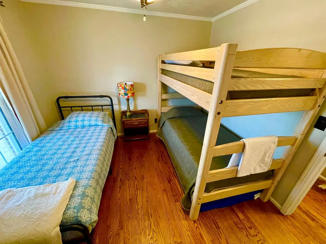 A bedroom with a single bed and a bunk bed, furnished with wooden floors and a bedside table with a lamp.