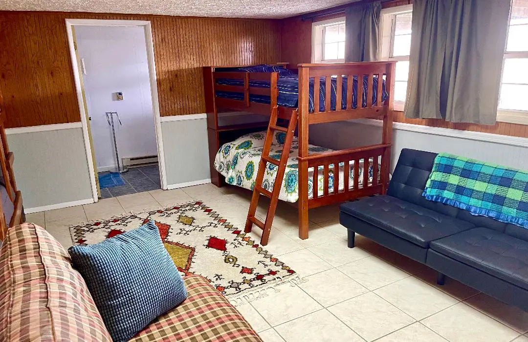 A modestly furnished living space with a bunk bed, a sofa, and patterned rugs on the floor.