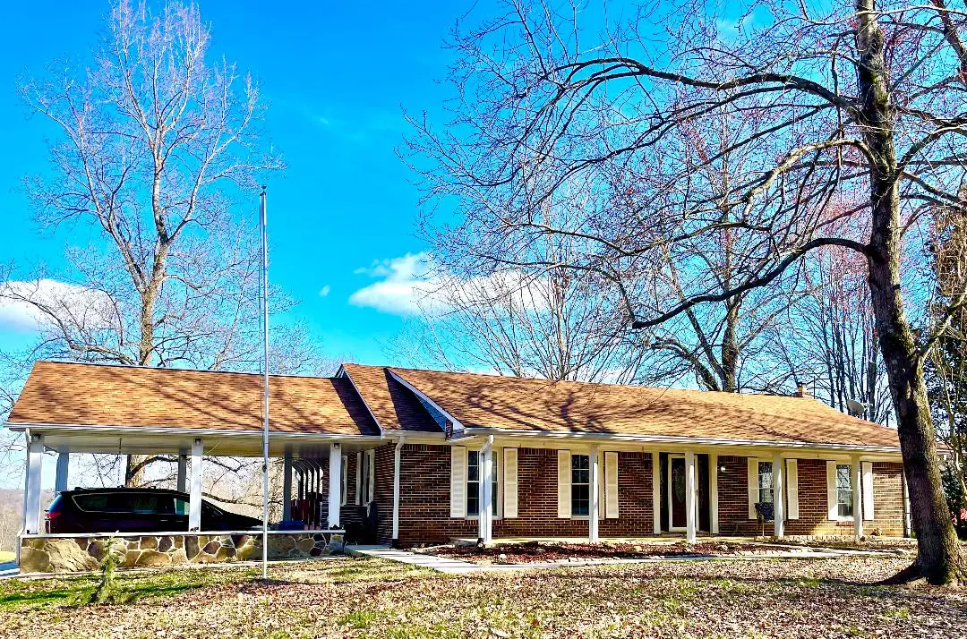 Single-story brick house with a covered porch and bare trees under a clear, blue sky.