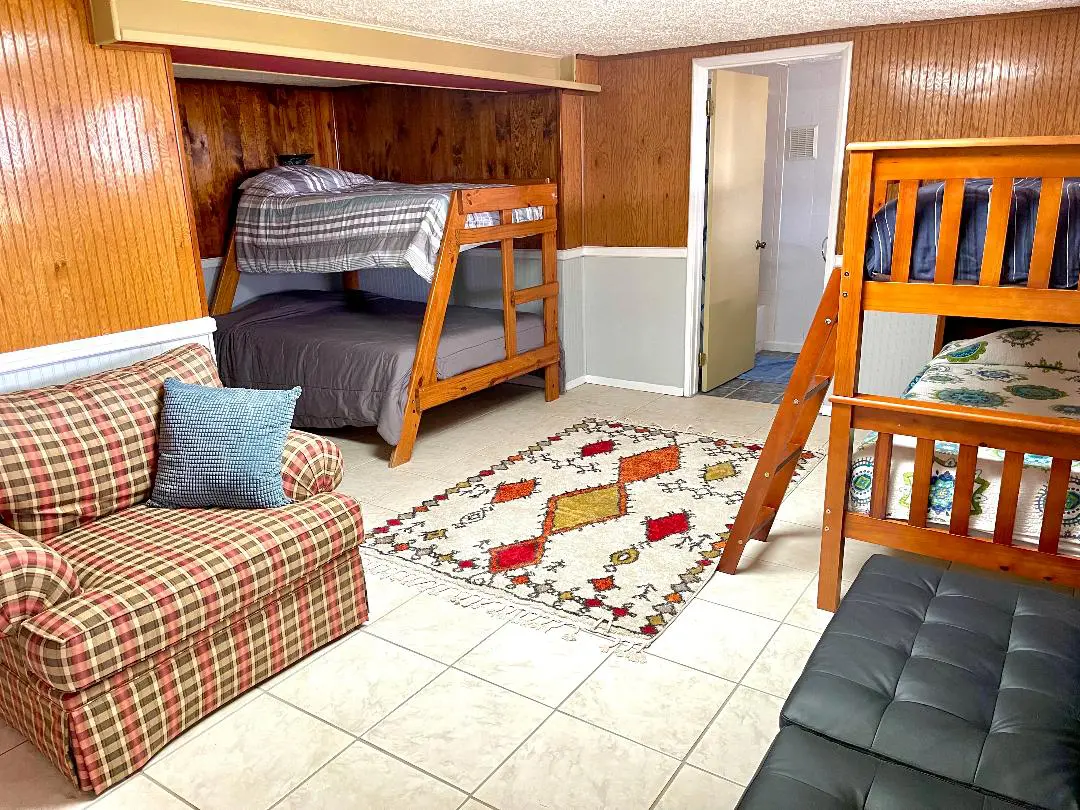 A cozy room with two bunk beds, a plaid sofa, a black leather seat, and a patterned area rug.