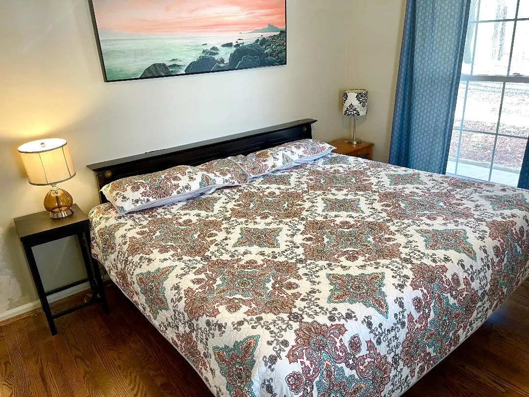 A neatly made bed with a paisley comforter in a bedroom with a coastal painting above the headboard.