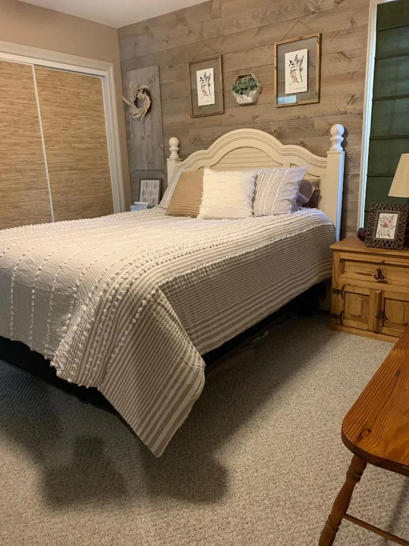 A neatly made bed with a white bedspread in a cozy bedroom with rustic wooden decor and wall art.