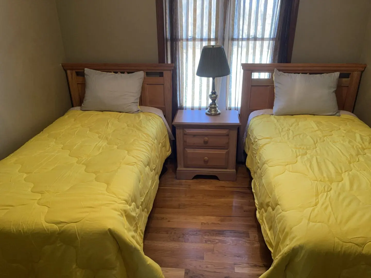 A bedroom with two single beds covered in yellow duvets and a wooden nightstand with a lamp between them.