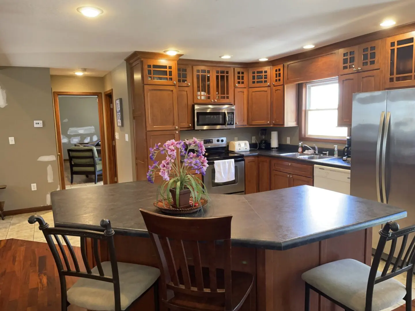 A modern kitchen interior with wooden cabinets, stainless steel appliances, and a floral centerpiece on the island.