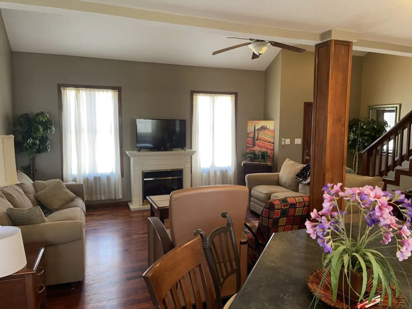 A cozy living room with a fireplace, comfortable seating, and a dining area with a view of a staircase and houseplants.