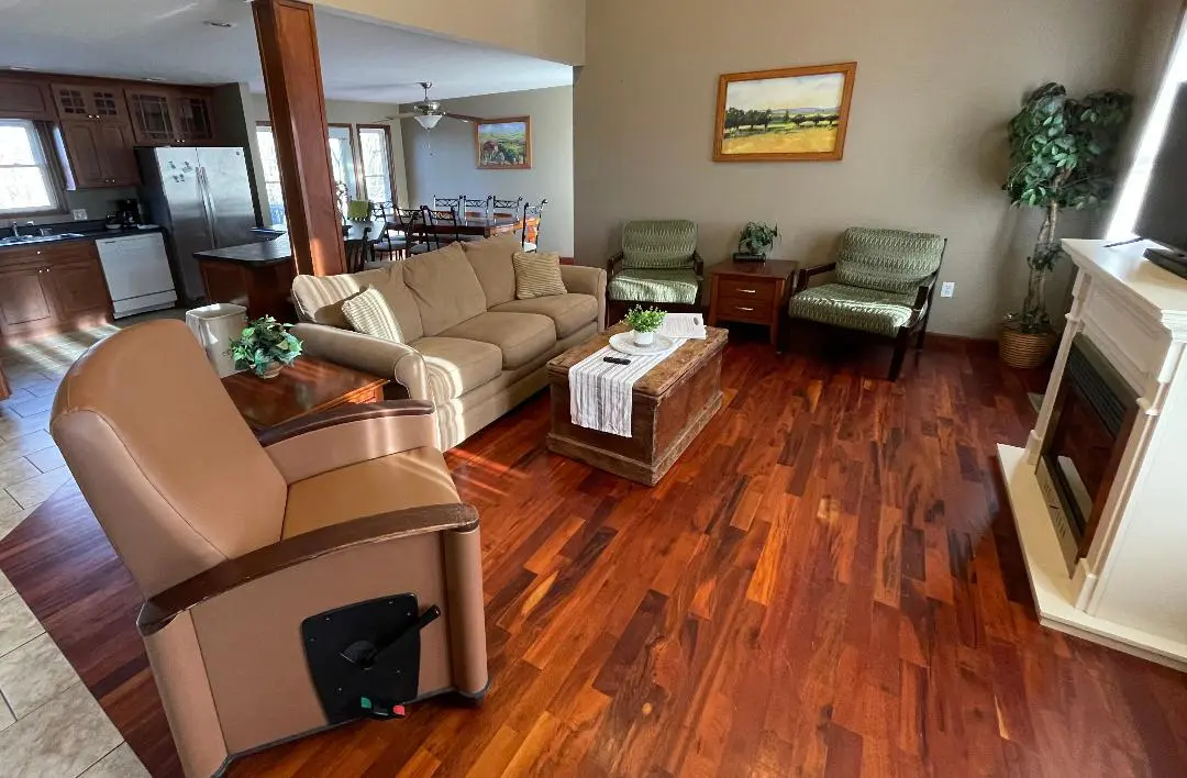 A well-kept living room with a beige sofa set, hardwood floors, and a view into the kitchen area.