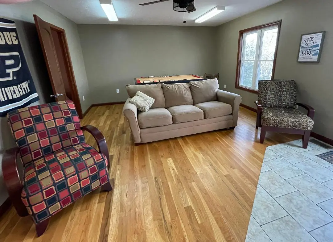 A cozy living space with a tan sofa, patterned chairs, and a billiard table in the background.