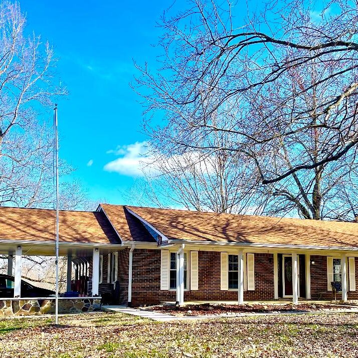 A single-story brick house with a covered porch and bare trees against a clear blue sky.