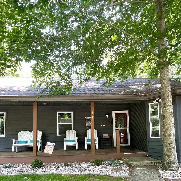 Cozy cabin with porch and surrounding trees.