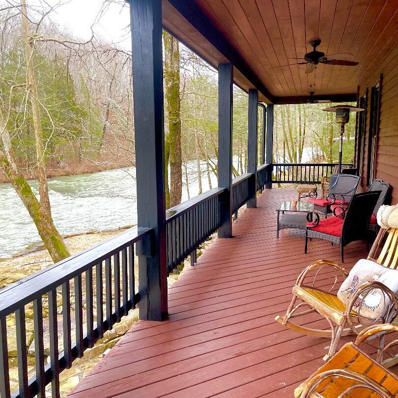 A cozy porch overlooking a river with seating and a ceiling fan.