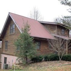 A log cabin in the woods with a red roof.